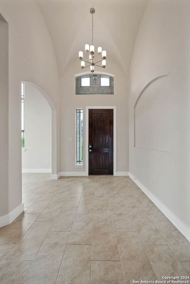 tiled entryway featuring an inviting chandelier, a wealth of natural light, and high vaulted ceiling