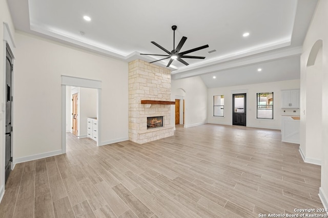 unfurnished living room with a tray ceiling, a fireplace, light wood-type flooring, and ceiling fan