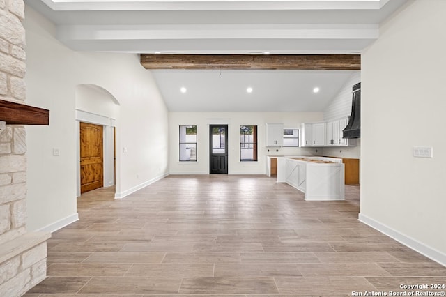 unfurnished living room featuring vaulted ceiling with beams and light wood-type flooring