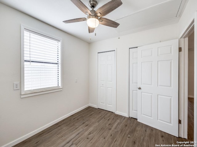 unfurnished bedroom featuring two closets, dark wood-type flooring, and ceiling fan