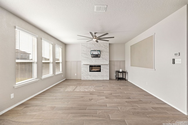 unfurnished living room featuring a textured ceiling, a tiled fireplace, light hardwood / wood-style floors, and ceiling fan