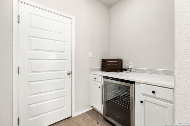 bar with white cabinets, light hardwood / wood-style floors, light stone counters, and beverage cooler