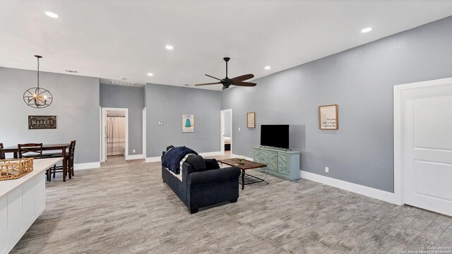 living room featuring ceiling fan with notable chandelier and light hardwood / wood-style flooring