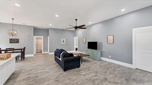 living room with ceiling fan with notable chandelier and light hardwood / wood-style flooring