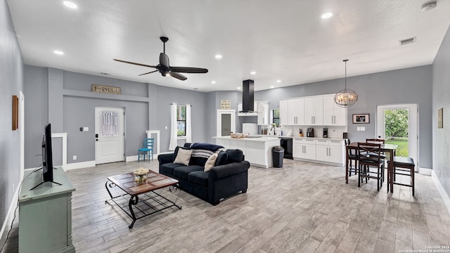 living room with ceiling fan with notable chandelier, light hardwood / wood-style flooring, and sink