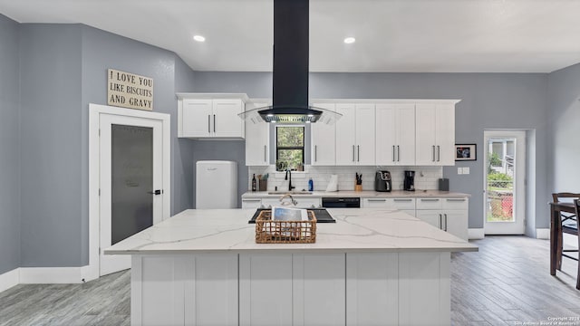 kitchen with plenty of natural light, a kitchen island, white cabinetry, and island range hood