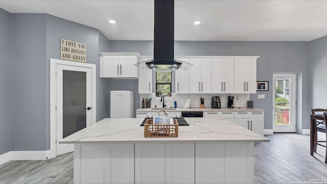 kitchen featuring white cabinetry, decorative backsplash, island exhaust hood, light stone counters, and black appliances