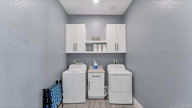 laundry room with cabinets, washing machine and dryer, and light wood-type flooring