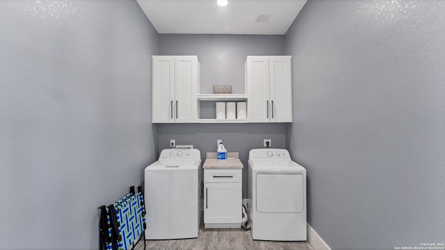 clothes washing area featuring cabinets, light hardwood / wood-style floors, and washer and dryer