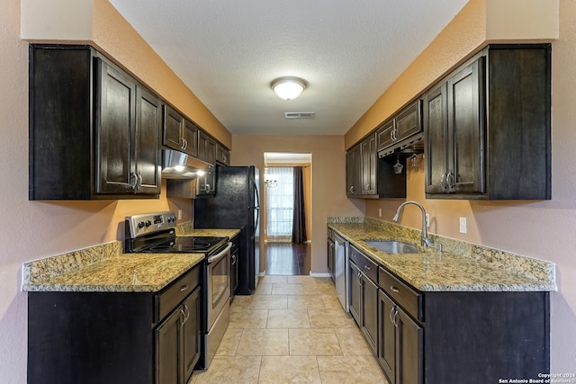 kitchen with appliances with stainless steel finishes, sink, light stone counters, dark brown cabinetry, and light tile patterned flooring