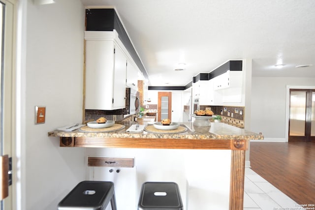 kitchen featuring a breakfast bar area, kitchen peninsula, decorative backsplash, and white cabinets