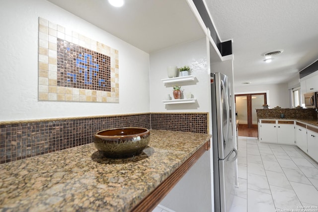 kitchen with tasteful backsplash, a textured ceiling, dark stone countertops, stainless steel appliances, and white cabinets