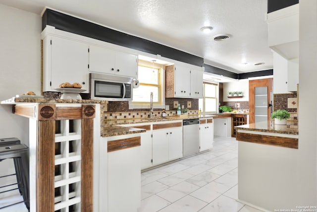 kitchen with appliances with stainless steel finishes, kitchen peninsula, decorative backsplash, dark stone countertops, and white cabinetry