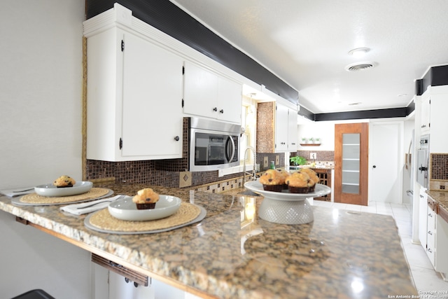 kitchen featuring light tile patterned flooring, white cabinetry, kitchen peninsula, light stone counters, and decorative backsplash