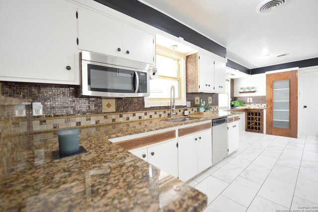 kitchen featuring sink, white cabinetry, stone countertops, appliances with stainless steel finishes, and backsplash