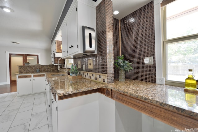 kitchen with kitchen peninsula, white cabinets, backsplash, light hardwood / wood-style floors, and sink