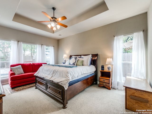 bedroom with a tray ceiling, light carpet, and ceiling fan