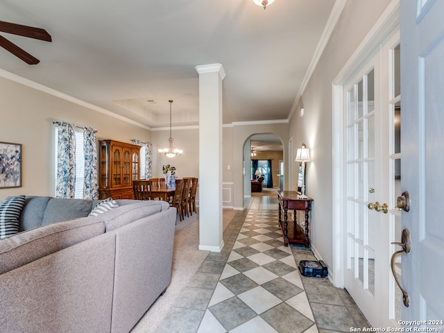 living room featuring ceiling fan with notable chandelier, crown molding, a tray ceiling, and light tile patterned floors