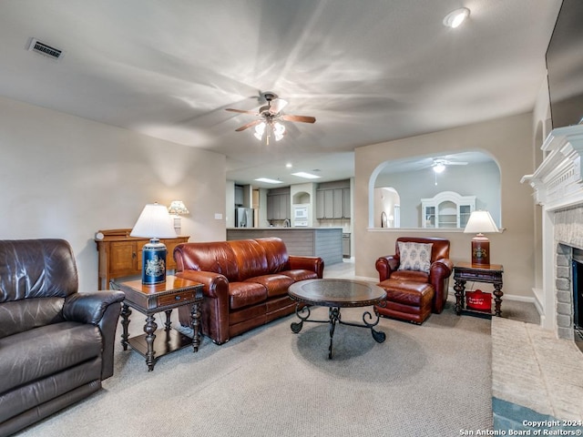 carpeted living room featuring arched walkways, visible vents, a fireplace, and ceiling fan