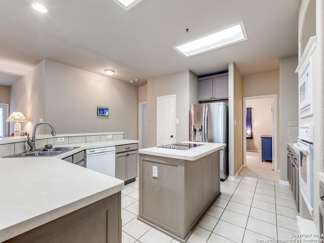 kitchen featuring white dishwasher, a kitchen island, a sink, and light tile patterned flooring