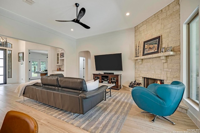 living room featuring light hardwood / wood-style flooring, a stone fireplace, french doors, crown molding, and ceiling fan