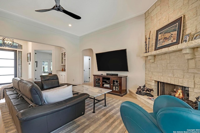 living room with ceiling fan, a stone fireplace, wood-type flooring, and ornamental molding