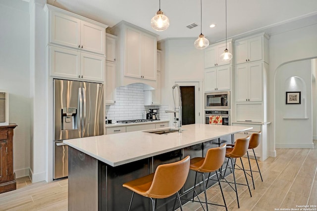 kitchen featuring stainless steel appliances, a center island with sink, white cabinets, decorative backsplash, and light wood-type flooring