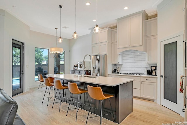 kitchen with appliances with stainless steel finishes, light hardwood / wood-style flooring, tasteful backsplash, pendant lighting, and an island with sink