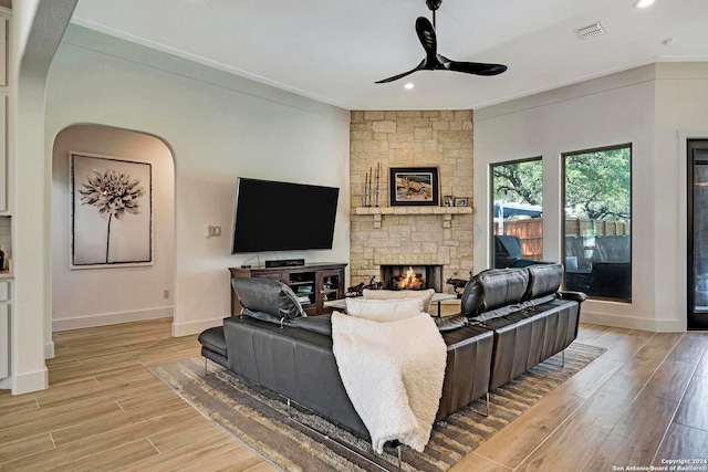 living room with light hardwood / wood-style floors, ceiling fan, a stone fireplace, and crown molding