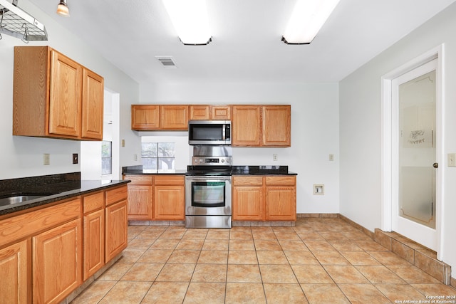 kitchen with dark stone counters, appliances with stainless steel finishes, and light tile patterned floors