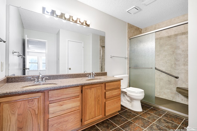 bathroom featuring a textured ceiling, dual bowl vanity, a shower with shower door, toilet, and tile patterned floors