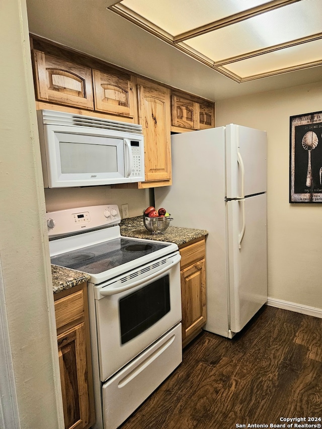 kitchen with dark stone counters, dark hardwood / wood-style flooring, and white appliances