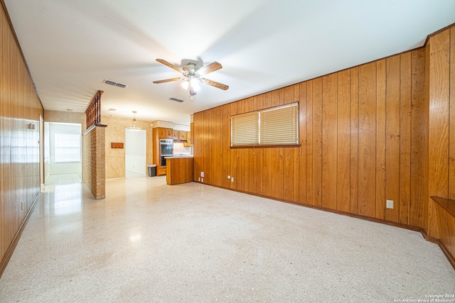 unfurnished living room with ceiling fan and wooden walls