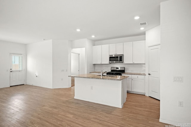 kitchen featuring appliances with stainless steel finishes, backsplash, light hardwood / wood-style floors, an island with sink, and white cabinetry