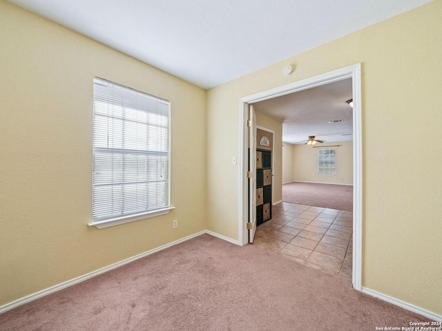 spare room featuring light tile patterned floors, baseboards, a ceiling fan, and light colored carpet