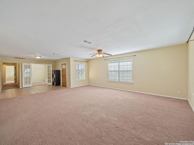 unfurnished living room featuring a textured ceiling, light colored carpet, visible vents, baseboards, and a ceiling fan