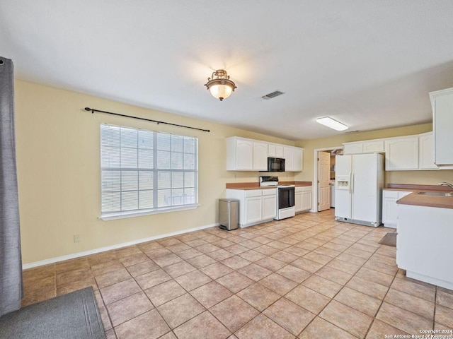 kitchen featuring visible vents, white cabinets, a sink, white appliances, and baseboards