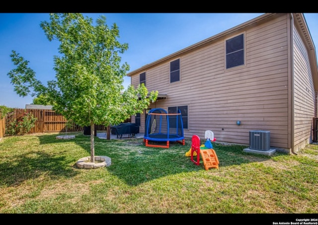 rear view of house with central AC unit, a trampoline, and a yard