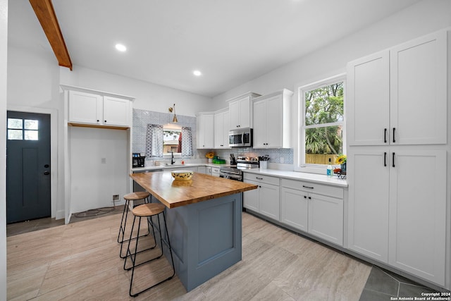 kitchen with wood counters, white cabinetry, tasteful backsplash, a center island, and stainless steel appliances