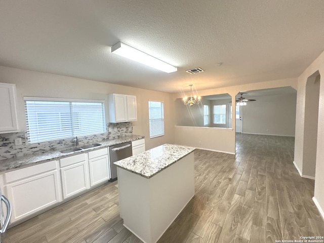 kitchen with sink, white cabinetry, light stone countertops, a kitchen island, and stainless steel dishwasher