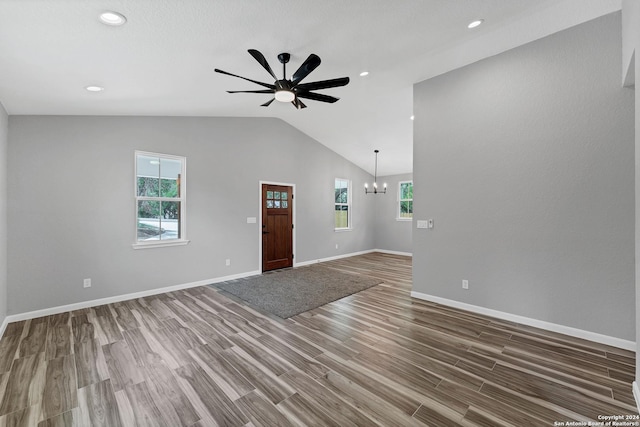 unfurnished living room featuring ceiling fan with notable chandelier, plenty of natural light, wood-type flooring, and vaulted ceiling