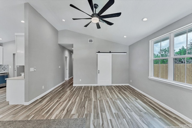 unfurnished living room with ceiling fan, lofted ceiling, a barn door, and light hardwood / wood-style floors