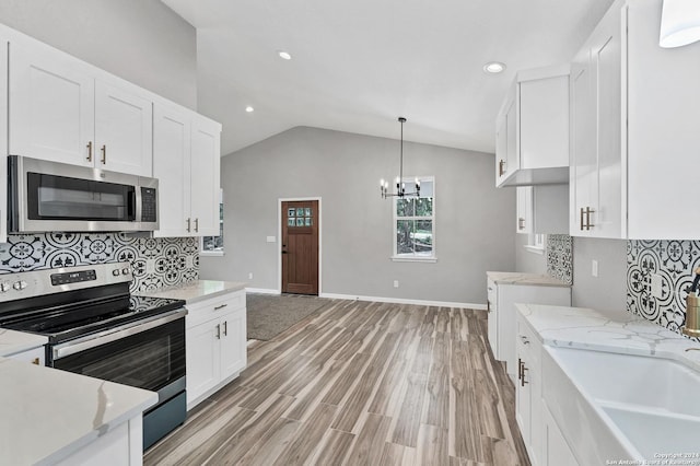 kitchen featuring vaulted ceiling, appliances with stainless steel finishes, white cabinets, hanging light fixtures, and light hardwood / wood-style flooring