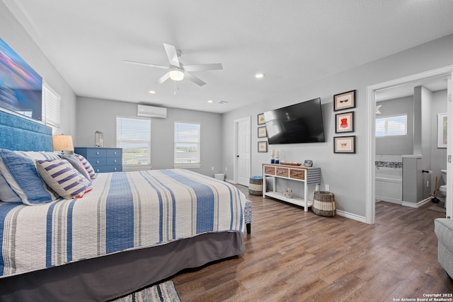 bedroom with connected bathroom, a wall mounted air conditioner, hardwood / wood-style floors, and ceiling fan