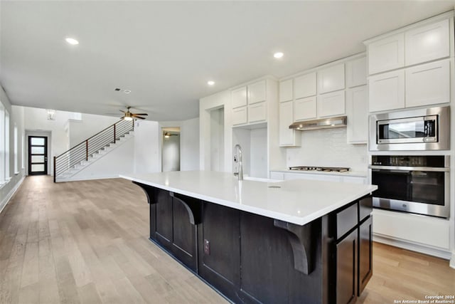 kitchen featuring stainless steel appliances, sink, an island with sink, and white cabinets