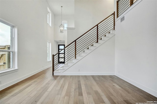 entrance foyer with an inviting chandelier, a towering ceiling, light hardwood / wood-style flooring, and a wealth of natural light