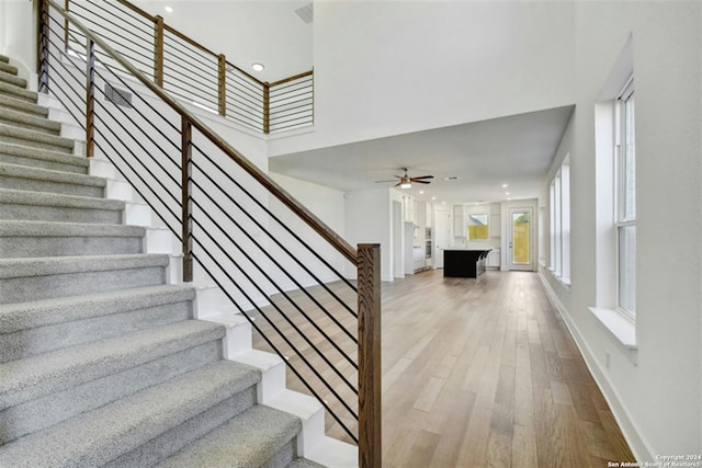 staircase featuring ceiling fan, a towering ceiling, and hardwood / wood-style floors