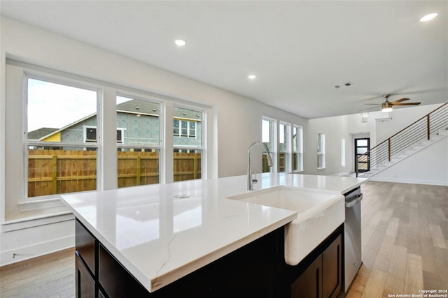 kitchen featuring an island with sink, sink, stainless steel dishwasher, and light wood-type flooring