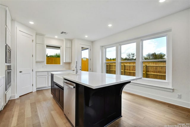 kitchen with sink, a kitchen island with sink, stainless steel appliances, white cabinets, and light wood-type flooring