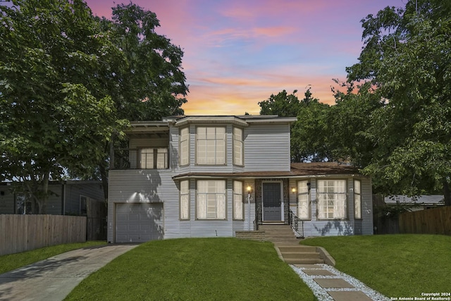 view of front facade featuring concrete driveway, an attached garage, fence, and a lawn